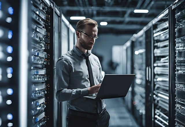Image of a man stood in a data centre looking at his laptop