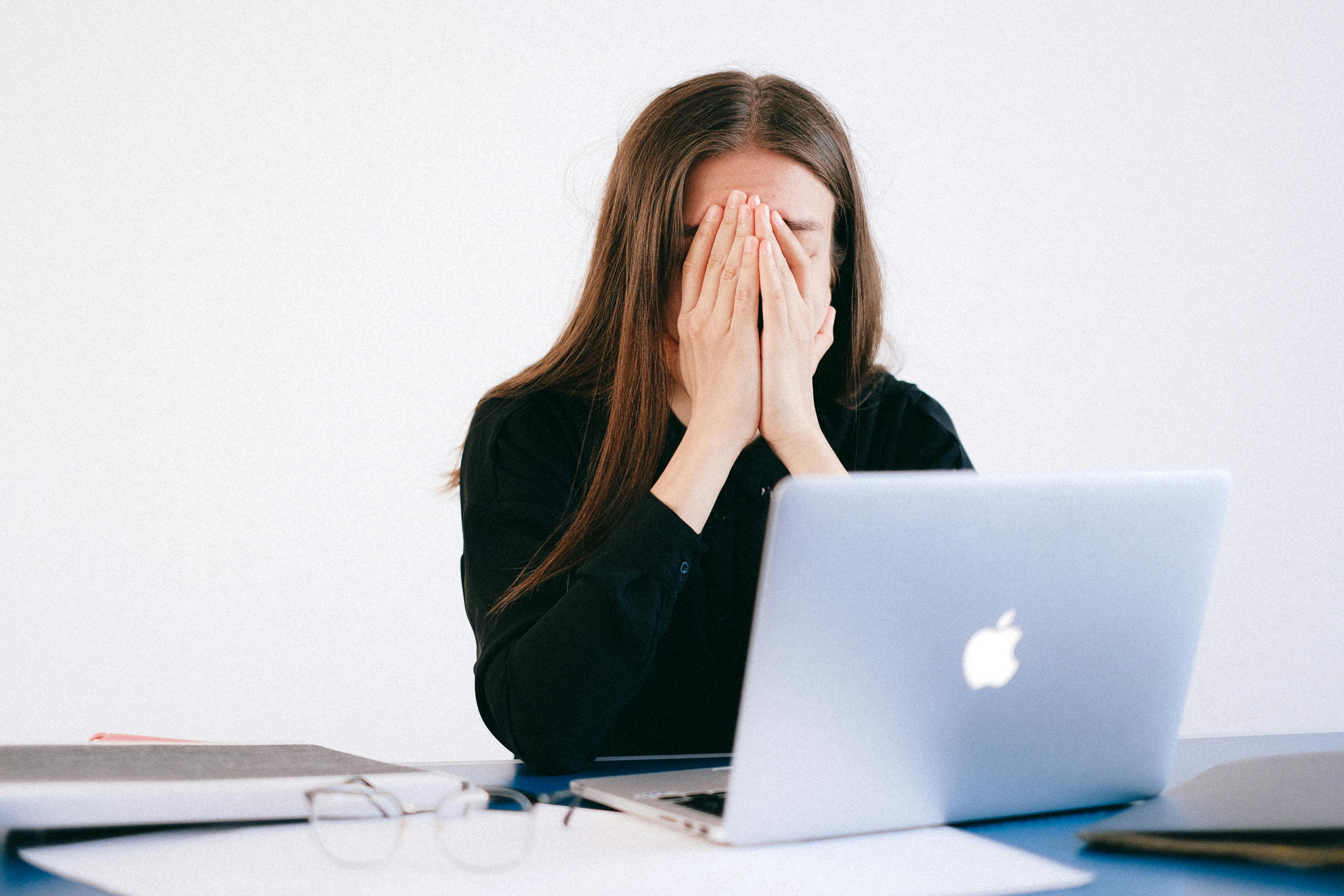 A stressed office worker with her head in her hands in front of her apple macbook